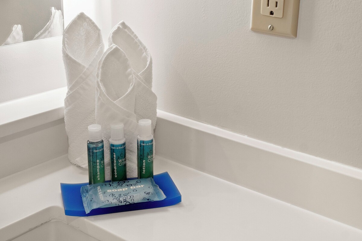 A bathroom with a white sink, a mirror, and toiletries including shampoo, conditioner, and soap.