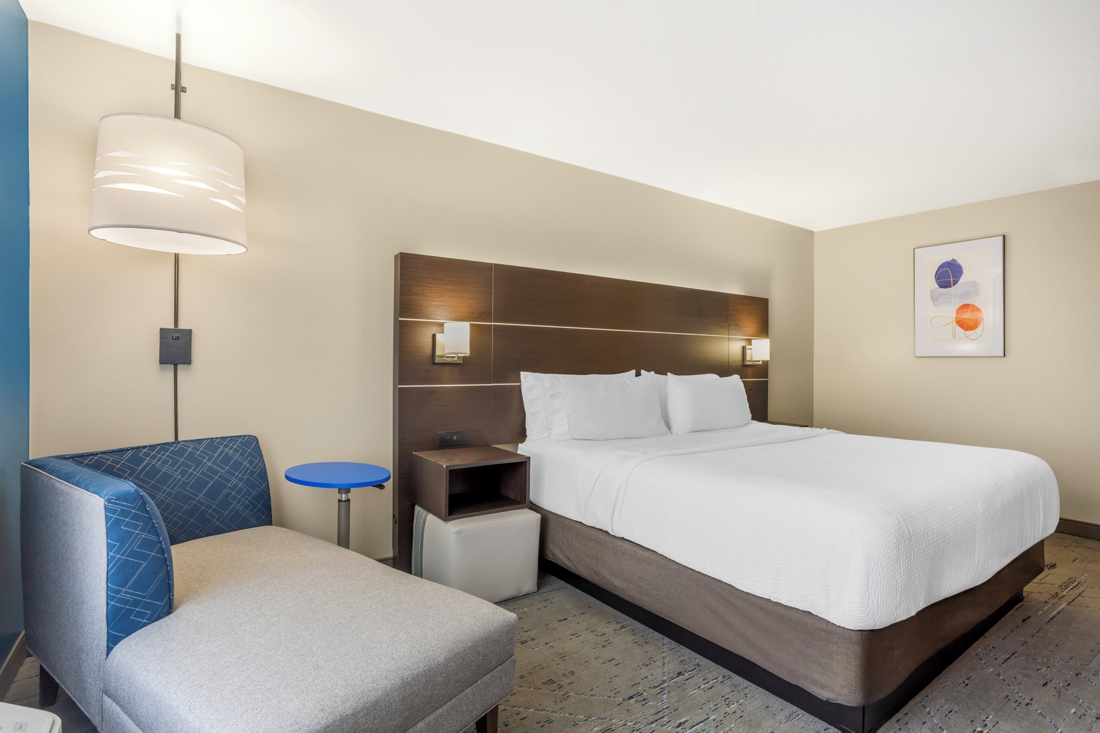 Ein Hotelzimmer mit einem Bett, einem Sessel, einem kleinen Tisch, einer Lampe und einer Wandleuchte.