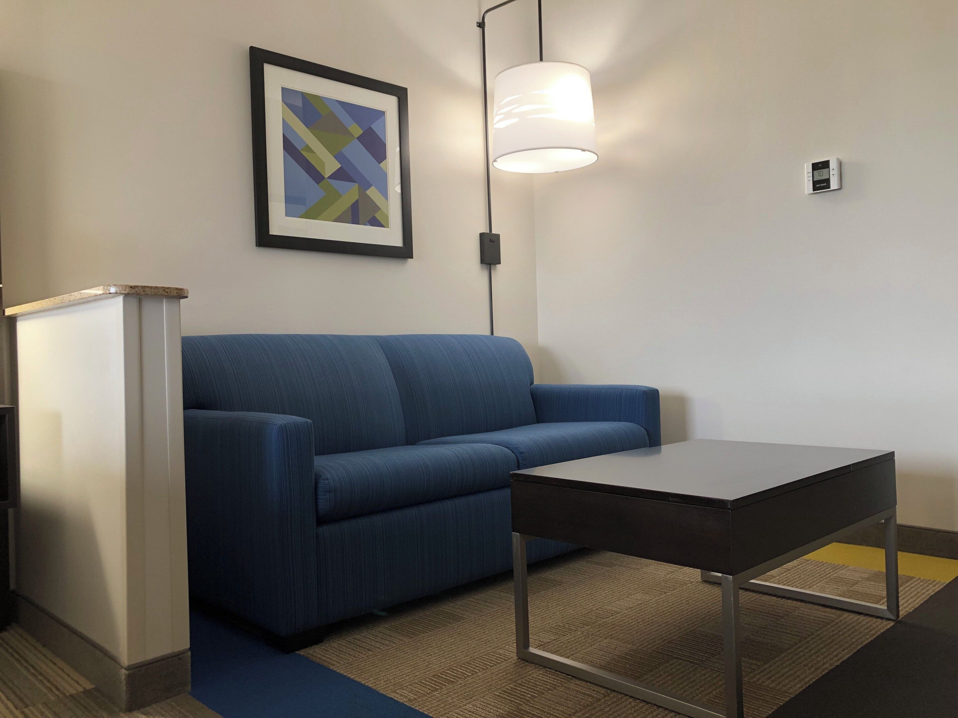 A room with a blue sofa, a small table, a framed abstract art piece, and a lamp.