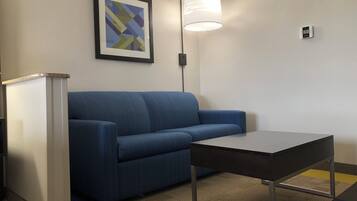 A room with a blue sofa, a small table, a framed abstract art piece, and a lamp.