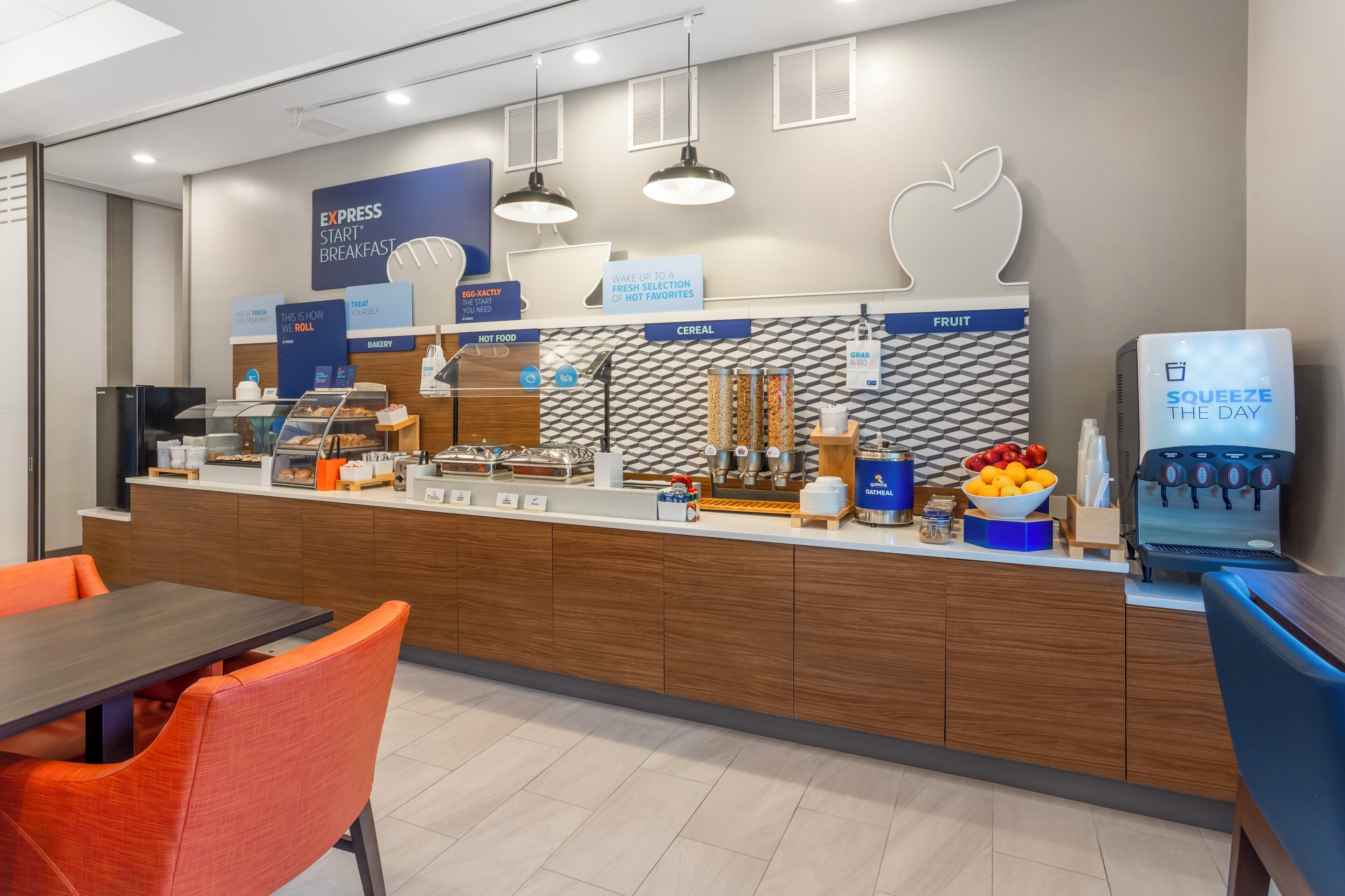 A modern breakfast area with a counter displaying various food options, a coffee machine, and seating arrangements.