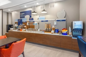 A modern breakfast area with a counter displaying various food options, a coffee machine, and seating arrangements. - Holiday Inn Express and Suites Newton by IHG (Newton)