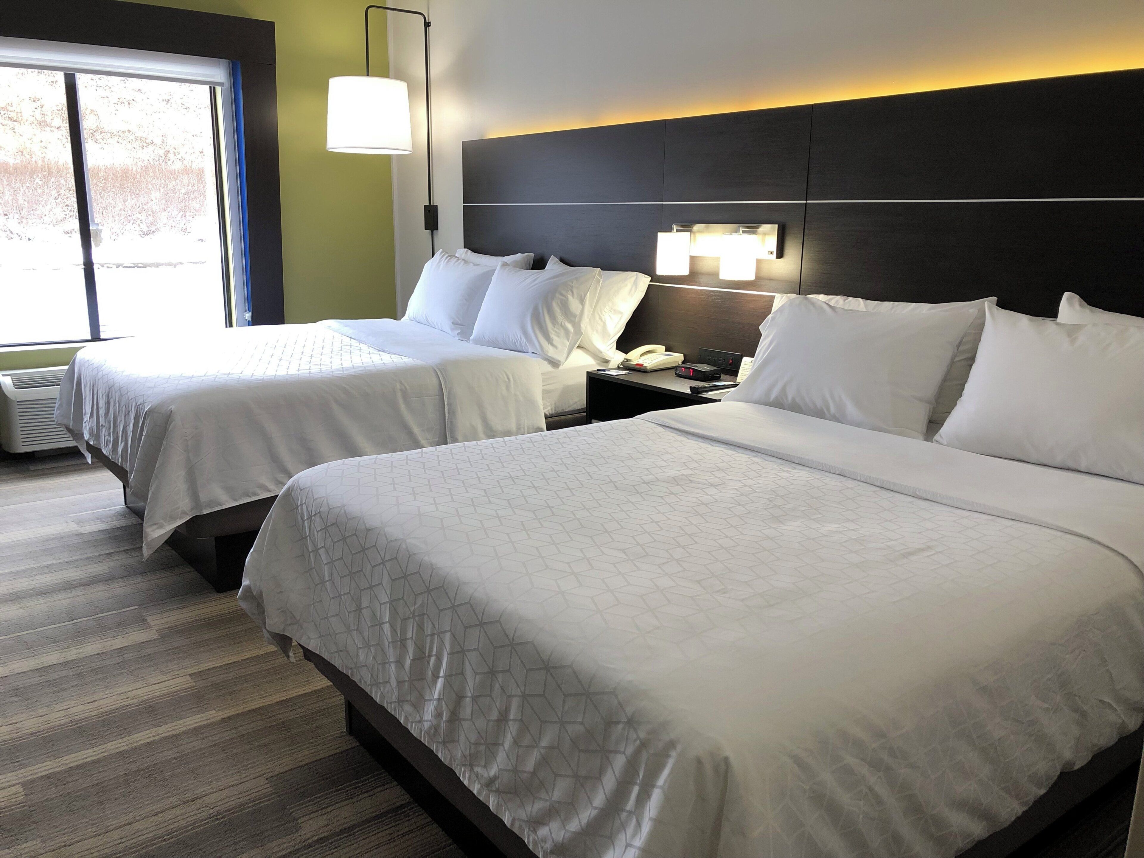 A hotel room with two beds, a nightstand with a phone and a lamp, and a window with a view.