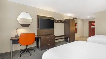 A hotel room with a desk, chair, bed, wardrobe, and a television.