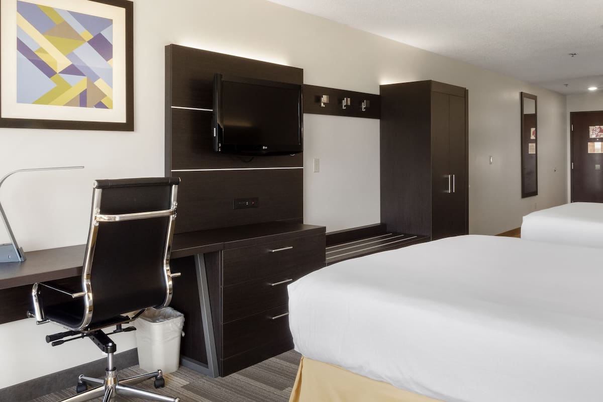 A hotel room with a bed, a desk with a chair, a TV, and a wardrobe.