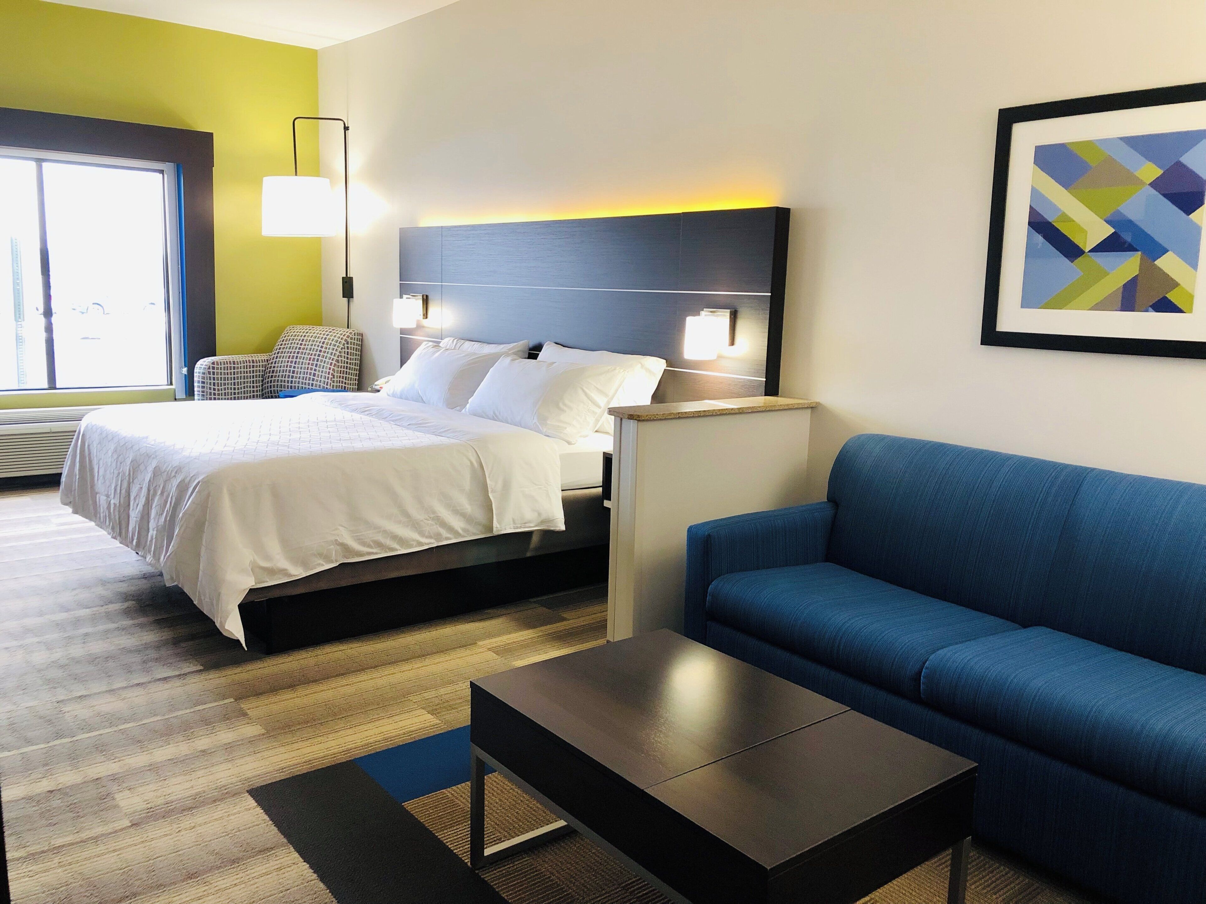 A hotel room with a bed, a blue sofa, a small table, and a wall-mounted lamp.