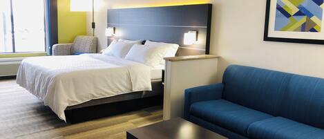 A hotel room with a bed, a blue sofa, a small table, and a wall-mounted lamp.