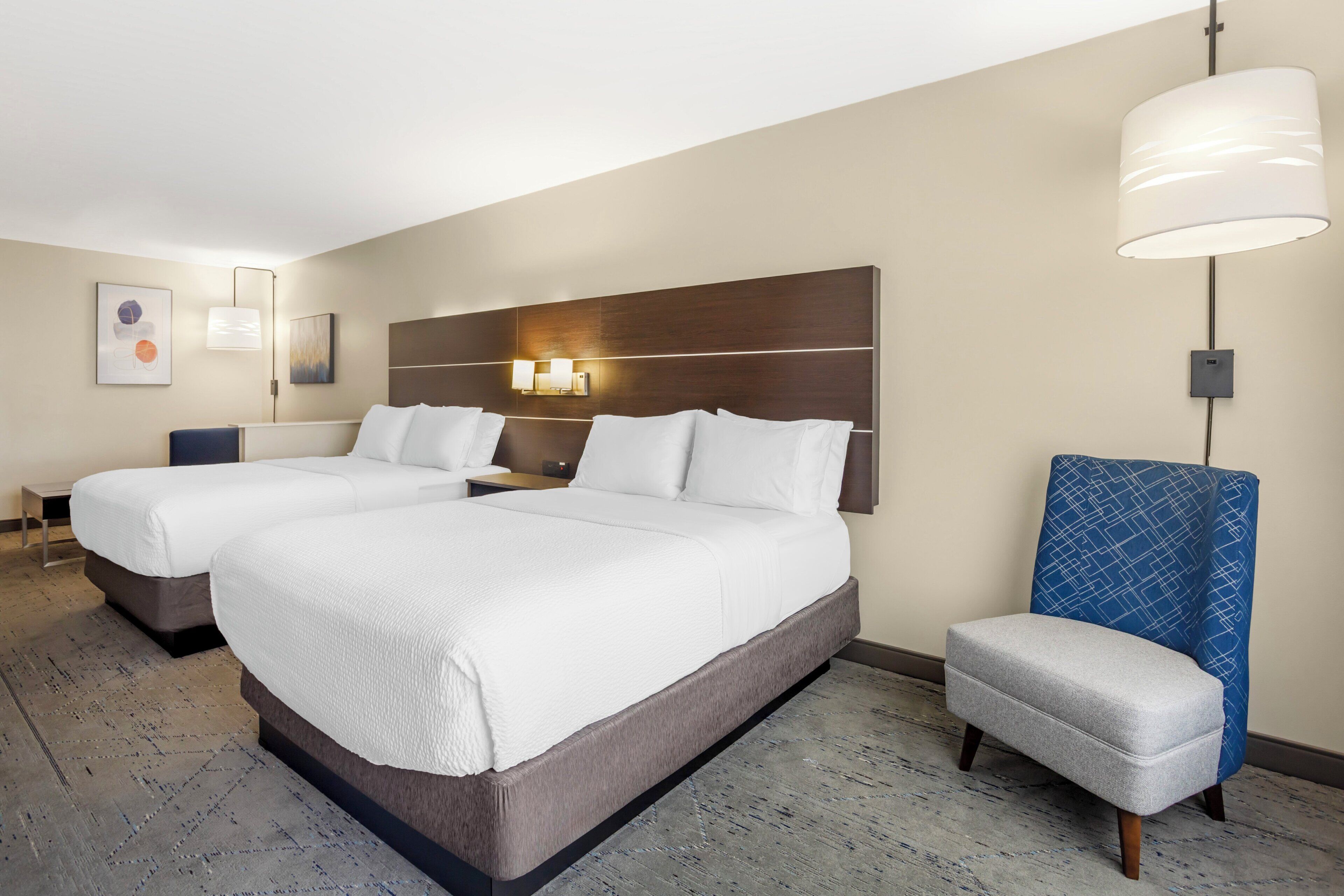 A hotel room with two beds, a desk, a chair, and a large window.