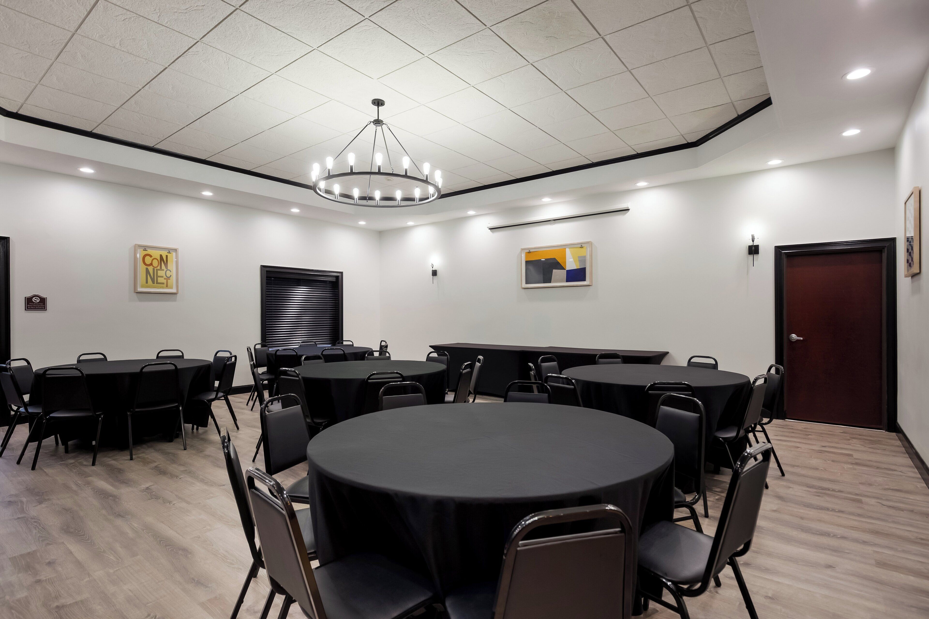 A conference room with round tables, black chairs, a chandelier, and artwork on the walls.