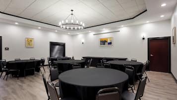 Une salle de conférence avec des tables rondes, des chaises noires, un lustre et des œuvres d’art accrochées aux murs.