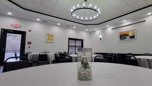 Una sala conferenze con tavoli rotondi, un lampadario e un vaso di vetro con elementi decorativi.