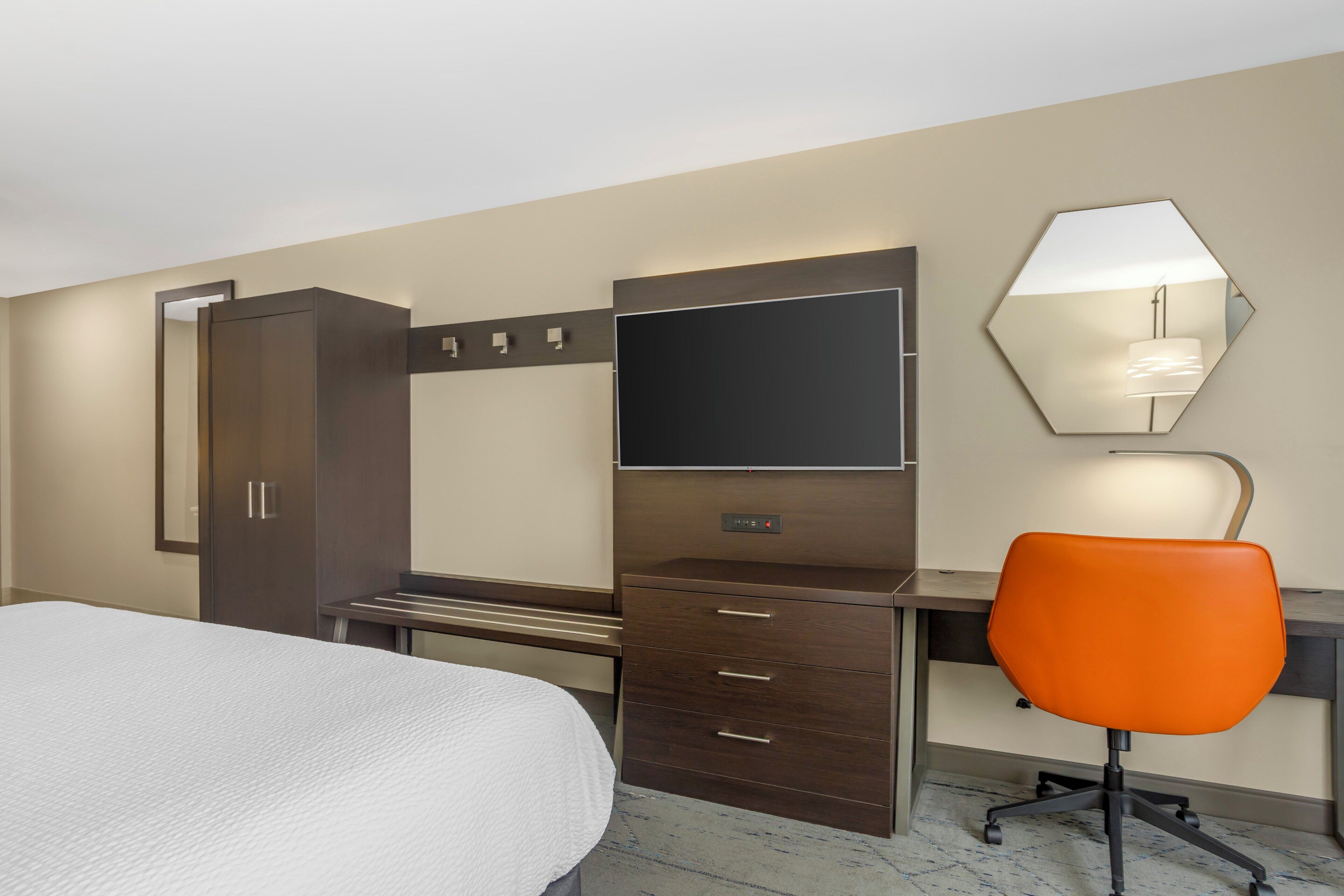 Une chambre d’hôtel comprenant un lit, un bureau avec une chaise, une armoire, un miroir et un téléviseur.