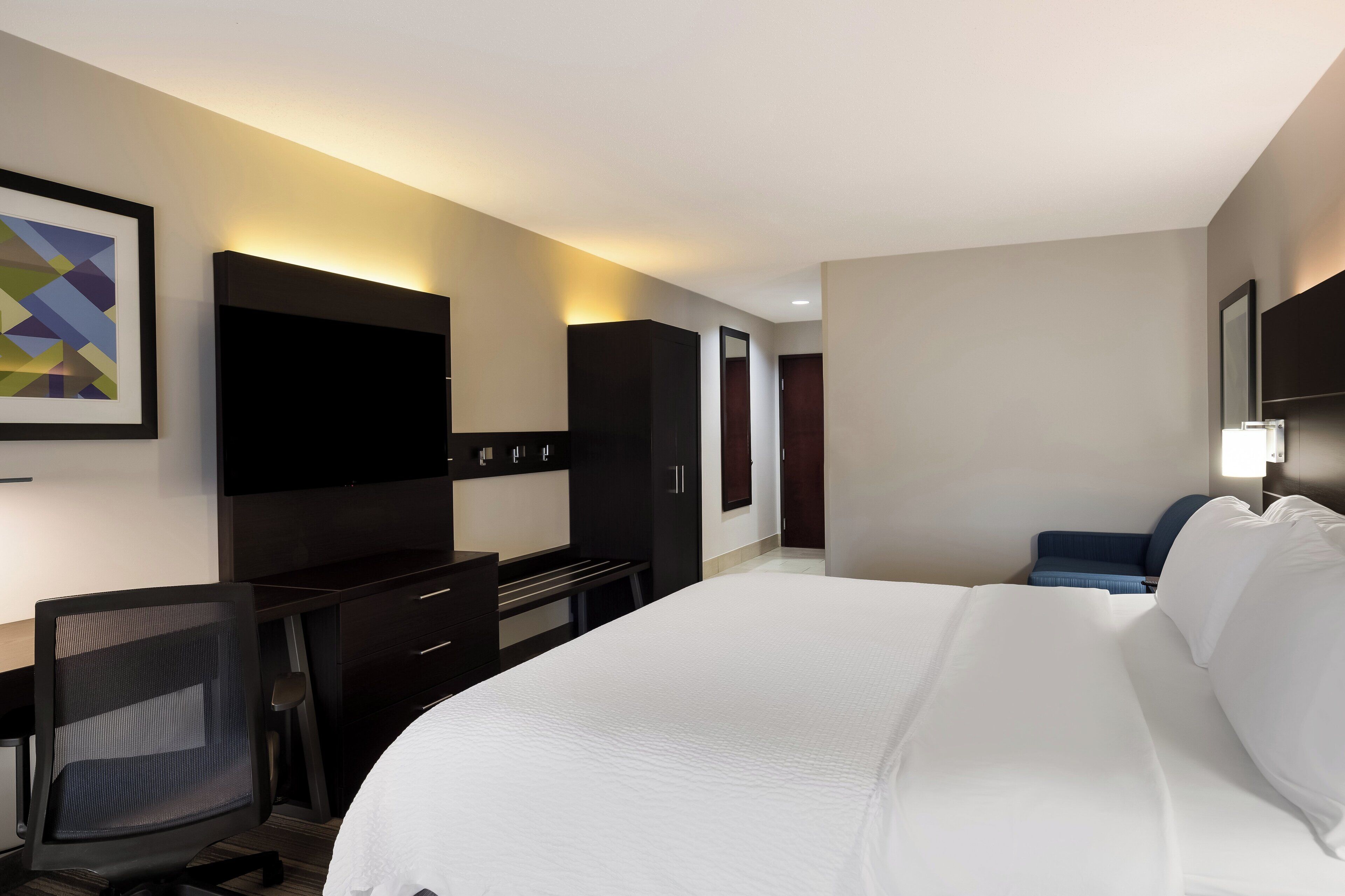 A hotel room with a large bed, a desk with a chair, a flat-screen TV, and a painting on the wall.