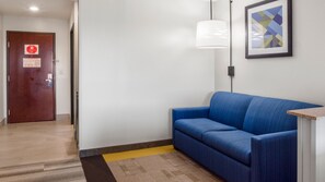 A hallway with a blue sofa, a door with a stop sign, and a framed abstract painting on the wall. - Holiday Inn Express and Suites Newton by IHG (Newton)
