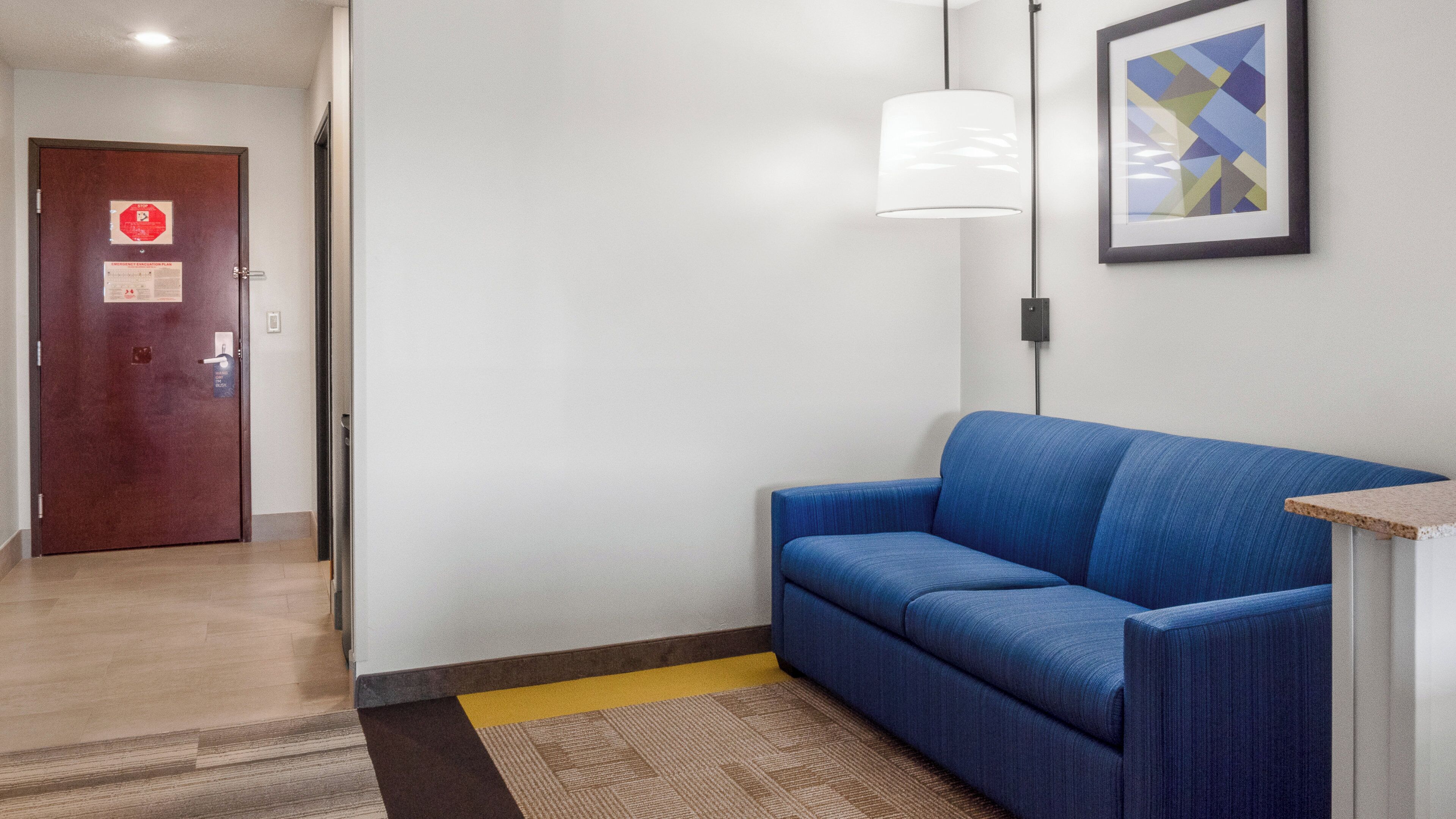 A hallway with a blue sofa, a door with a stop sign, and a framed abstract painting on the wall.
