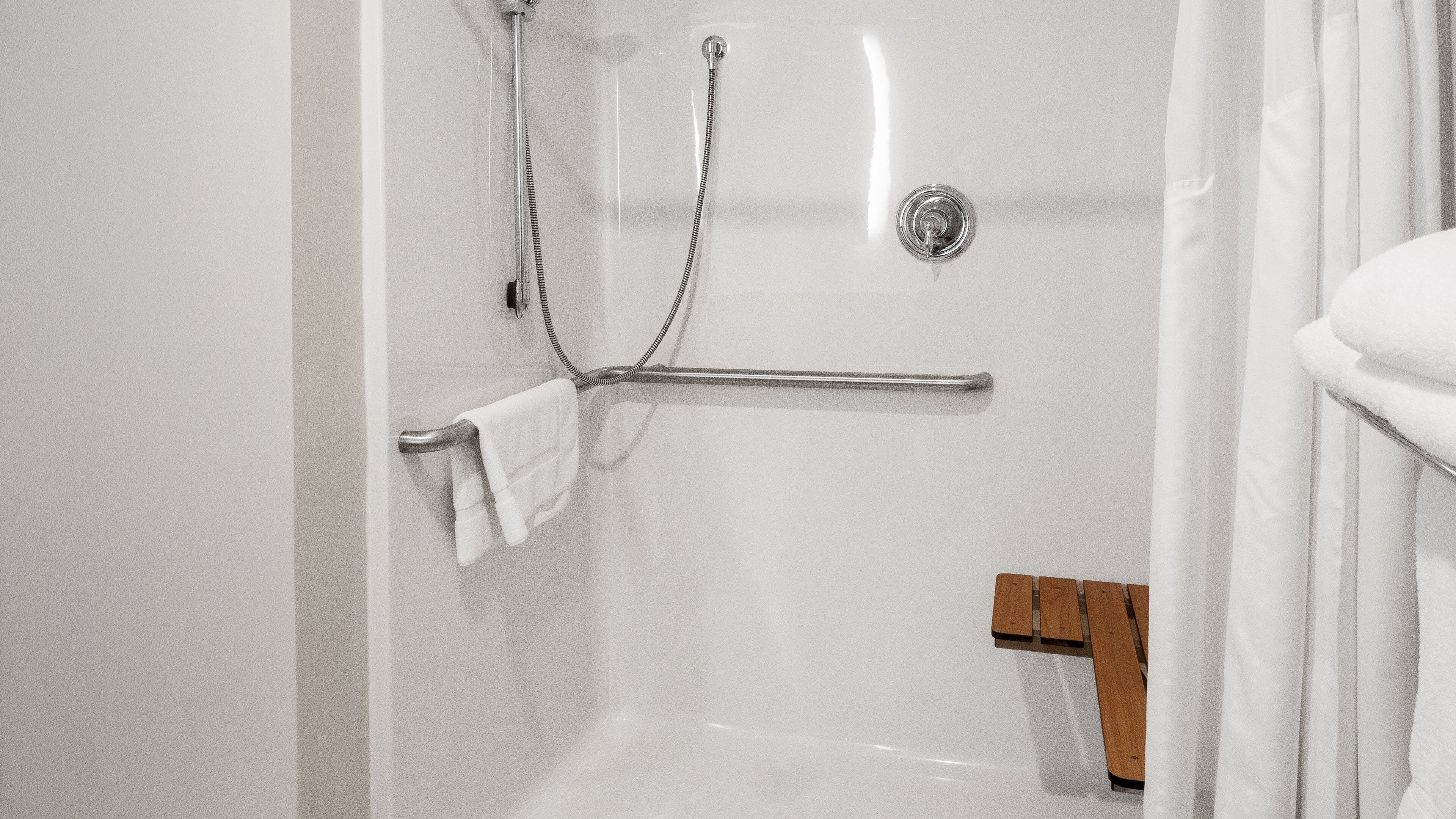 A white bathroom with a shower, a towel rack, and a wooden bench.
