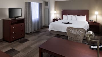 A hotel room with a large bed, a desk, a chair, a TV, and a lamp.