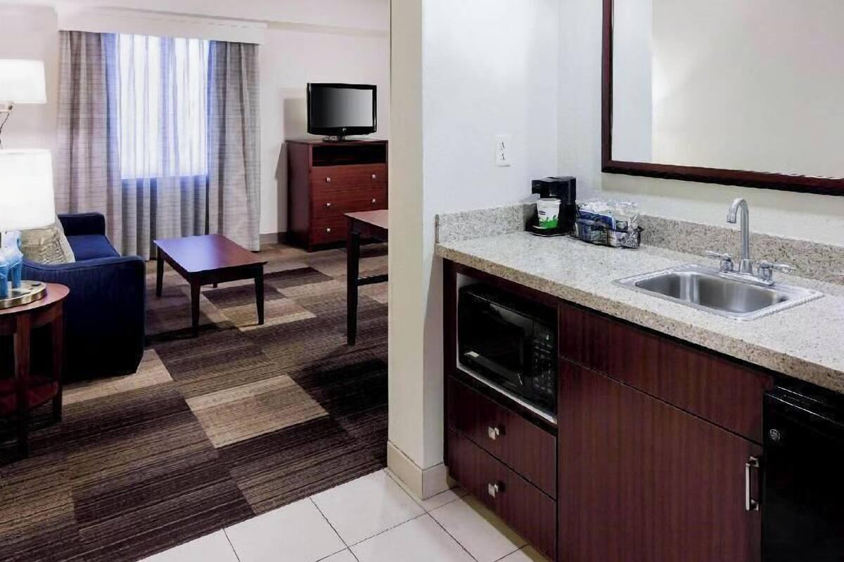 Habitación de hotel compacta con kitchenette, zona de comedor, televisor y un espejo grande.