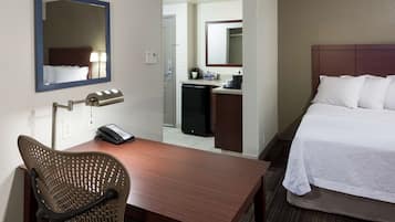 Ein Hotelzimmer mit einem Holztisch, einem Stuhl, einem Bett, einem Spiegel und einer Küchenzeile.