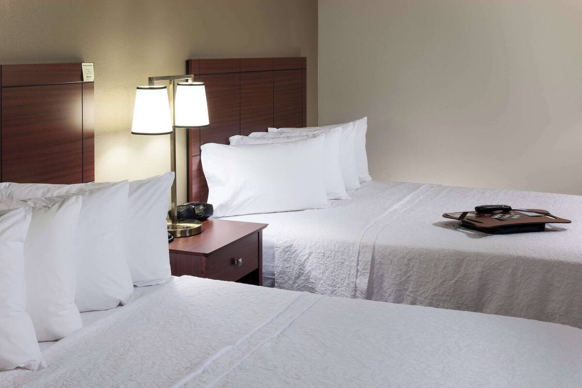 A hotel room with two beds, a nightstand, and a lamp.