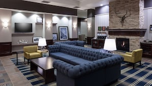 A modern hotel lobby with a large sectional sofa, two armchairs, a flat-screen TV, a fireplace, and a stone accent wall.