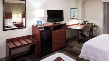 A hotel room with a bed, desk, chair, TV, refrigerator, and a mirror.