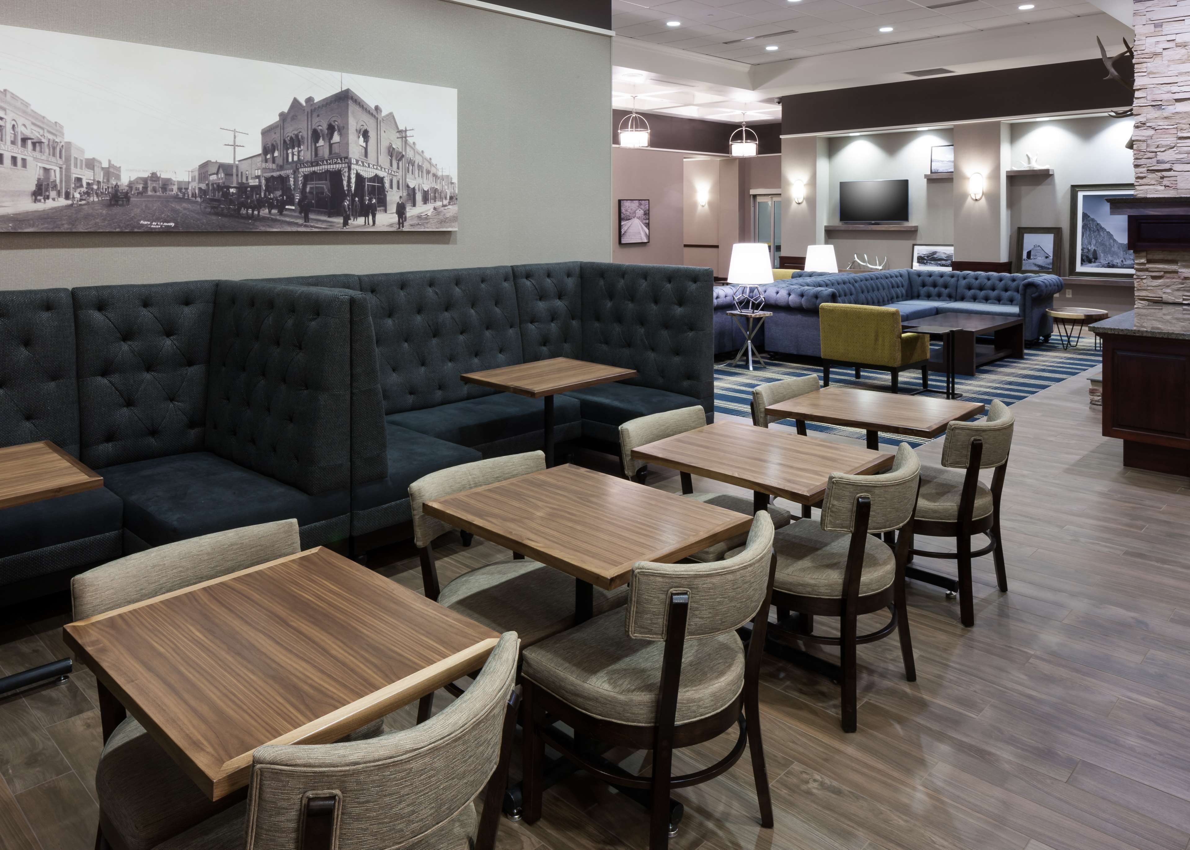 A modern hotel lobby with a large dark sofa, multiple wooden tables, and a seating area with a blue couch and yellow chairs.