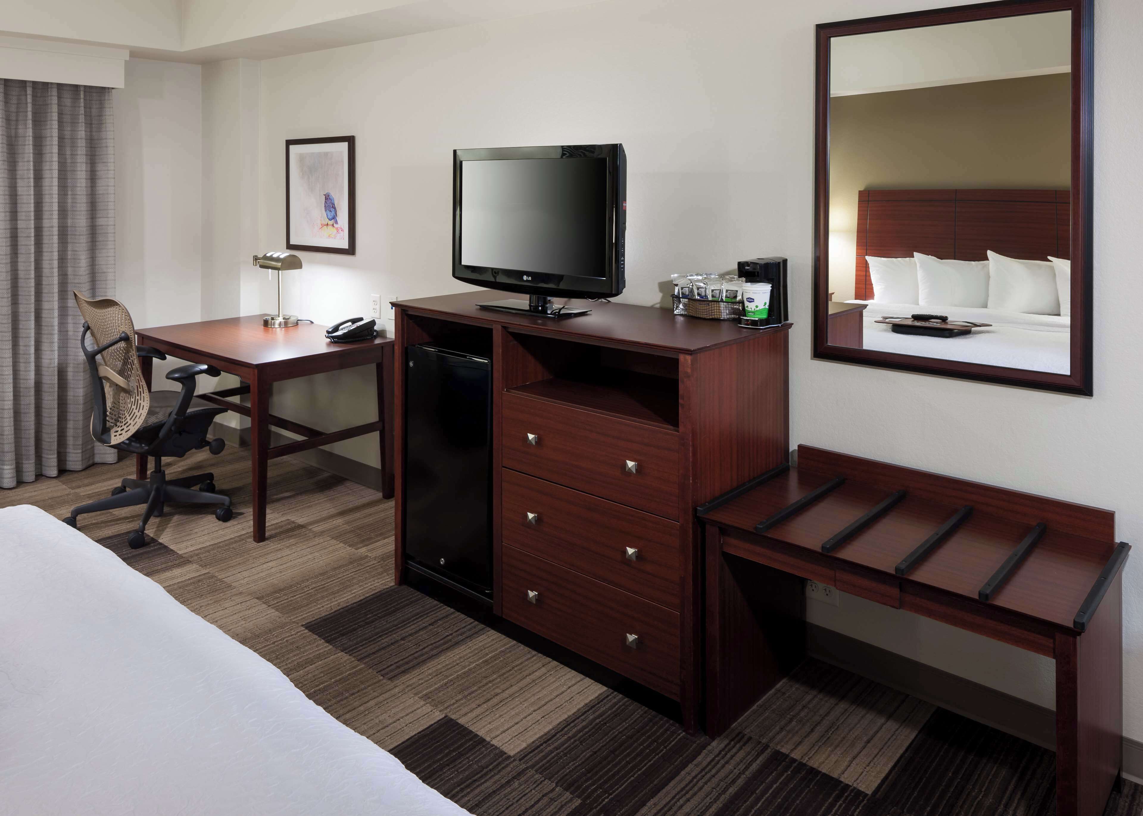 Ein Hotelzimmer mit einem Bett, einem Schreibtisch mit Computer, einem Fernseher, einem Schminktisch und einem Nachttisch.