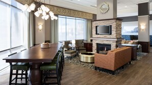 A hotel room with a dining area, a fireplace, a TV, and a seating area with a view of the city.