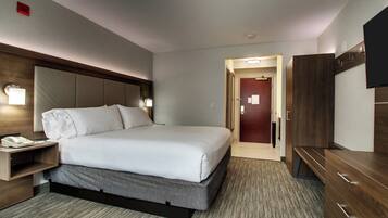 A hotel room with a bed, bedside table, lamp, and a television.
