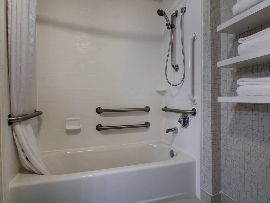A white bathtub with grab bars, a showerhead, and a towel rack.