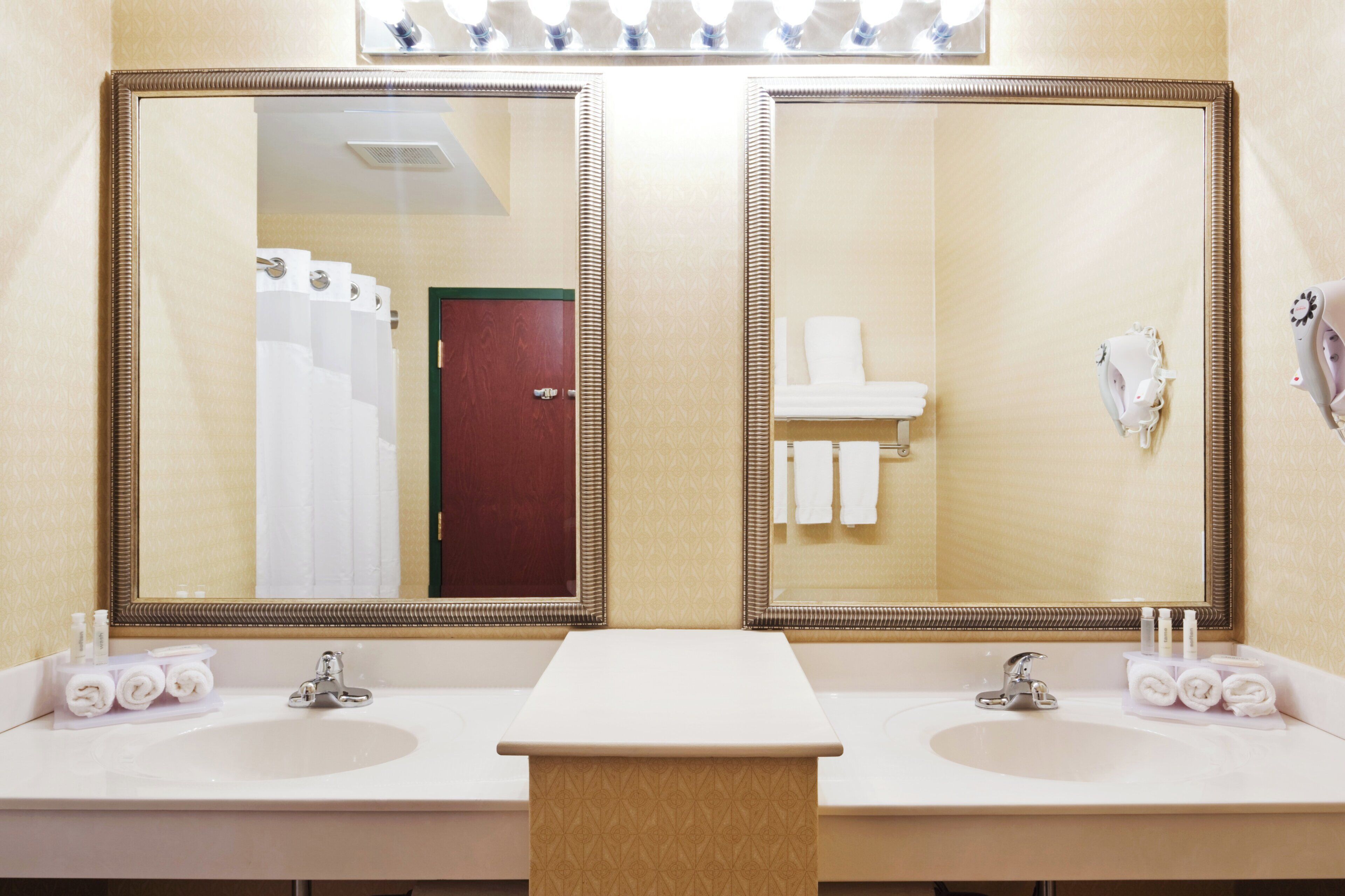 Casa de banho de hotel com duas pias, um espelho e um porta-toalhas.
