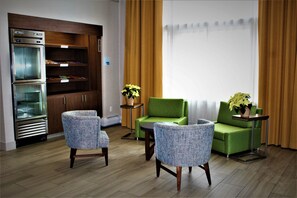 Una sala de estar con kitchenette, dos sillones, un sofá, una mesita y una planta en maceta.