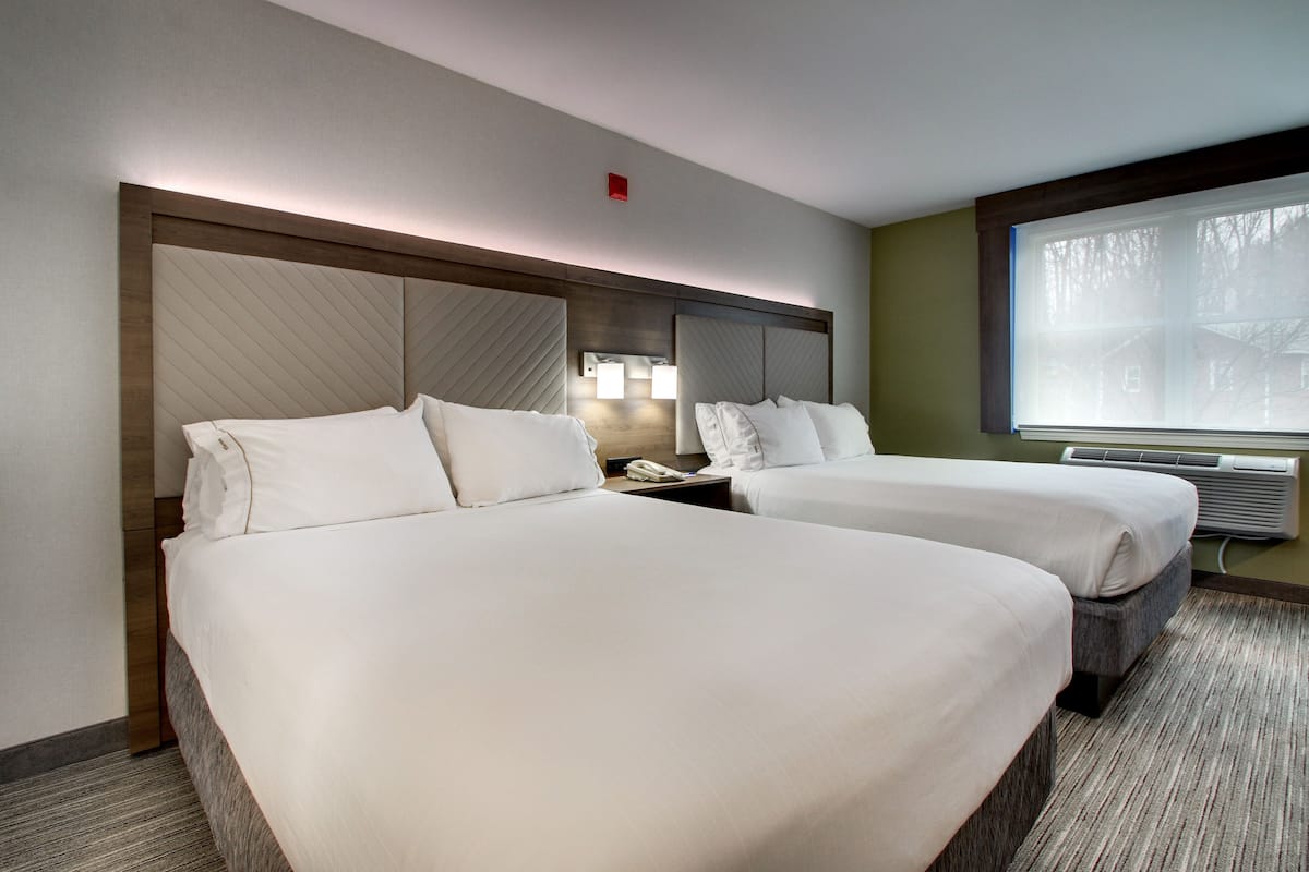 A hotel room with two beds, a large window, and a wall-mounted heater.