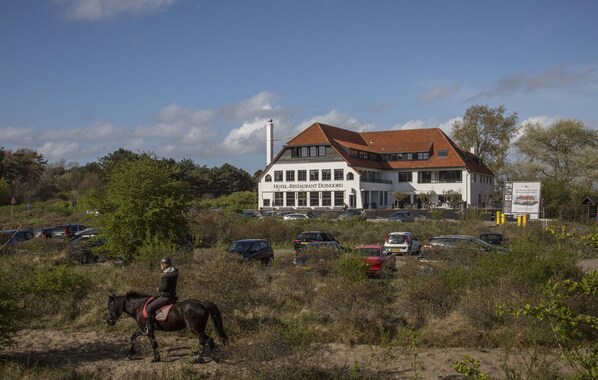 A building labeled "Hotel-restaurant Duinoord" with a red-tiled roof, surrounded by parked cars and vegetation.