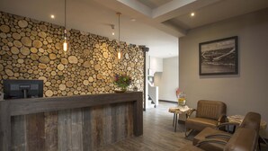 A reception area with a wooden reception desk, a stone wall, and a framed picture on the wall. - Fletcher Boutique Hotel Duinoord (Wassenaar)
