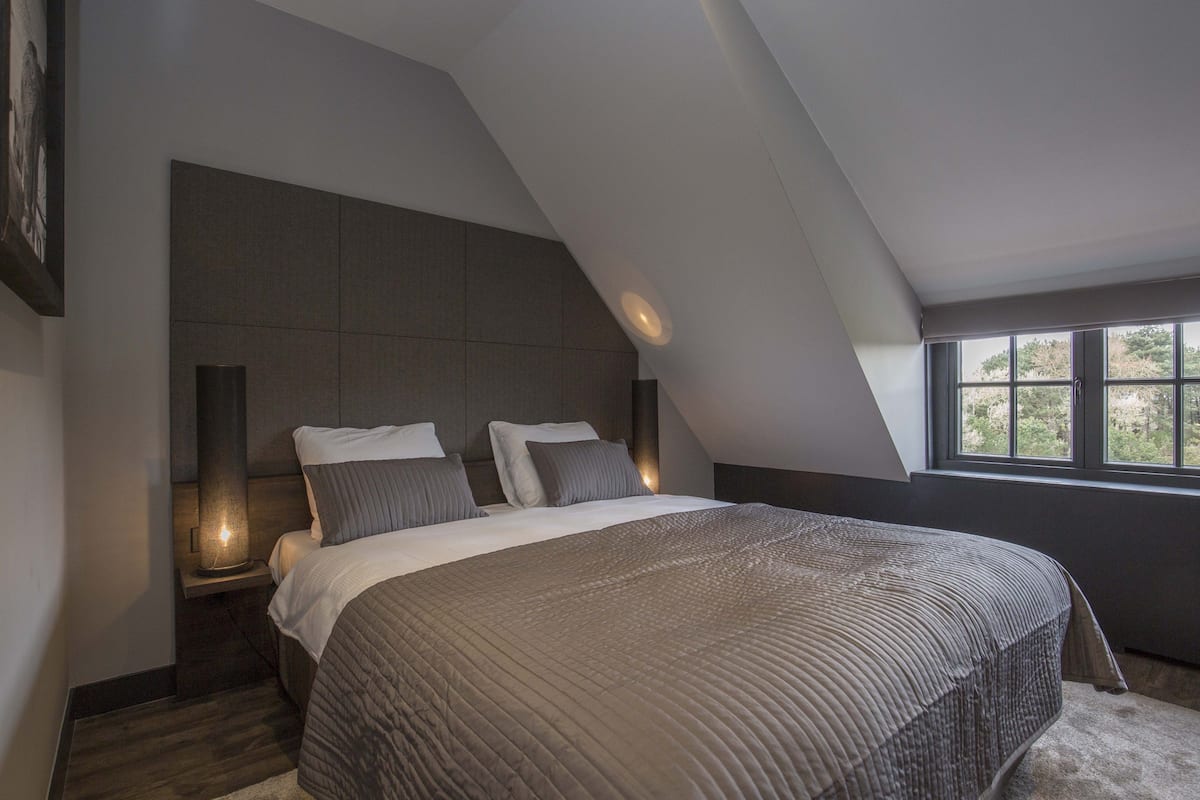 A modern bedroom with a large bed, a sloped ceiling, and a window providing a view of the outdoors.