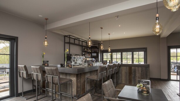 A bar area with stools, a bar counter, and hanging light fixtures. - Fletcher Boutique Hotel Duinoord (Wassenaar)