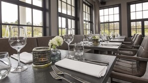 A dining area with tables set for a meal, large windows, and a view of the outdoors. - Fletcher Boutique Hotel Duinoord (Wassenaar)