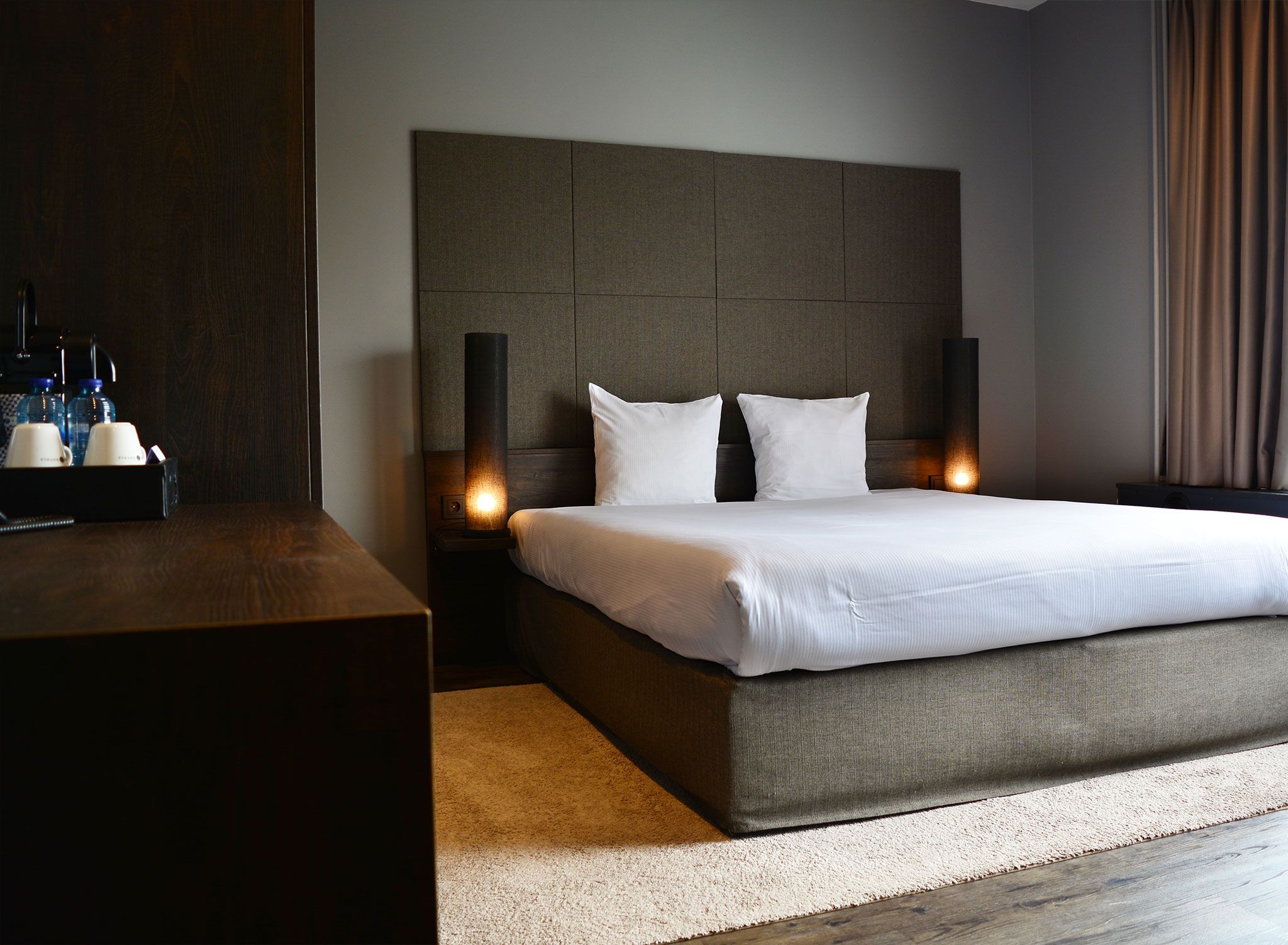 A modern hotel room with a large bed, a wooden nightstand, and two bedside lamps.