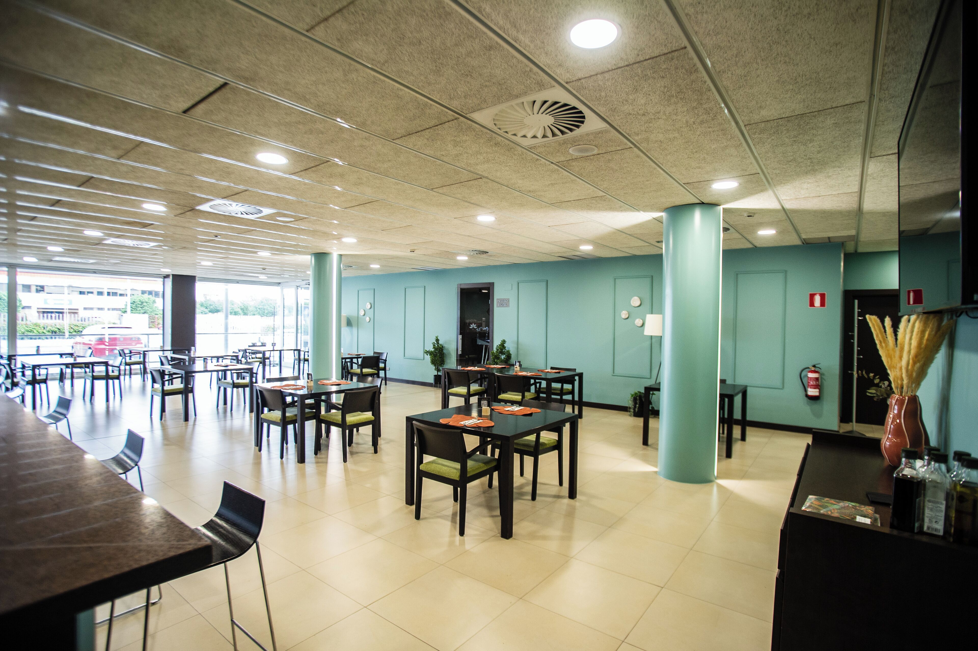 A spacious indoor area with multiple tables and chairs, a reception desk, and a view of the outside.