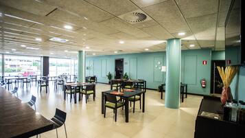 A spacious indoor area with multiple tables and chairs, a reception desk, and a view of the outside.