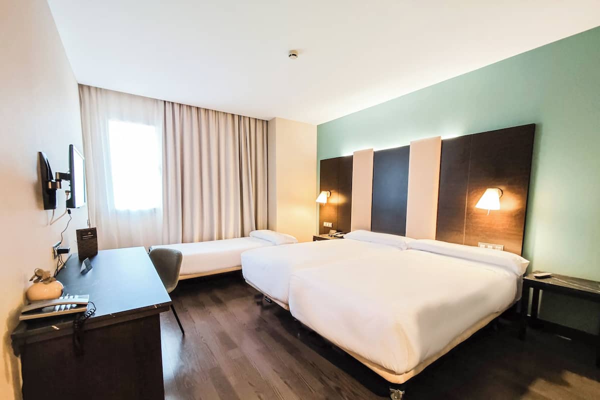 A hotel room with two beds, a desk, and a chair.