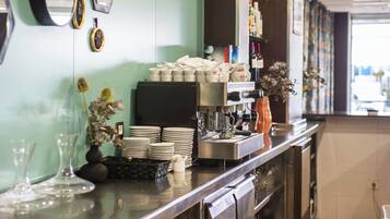 Zona de bar amb una màquina de cafè, plats apilats i un vas amb flors.