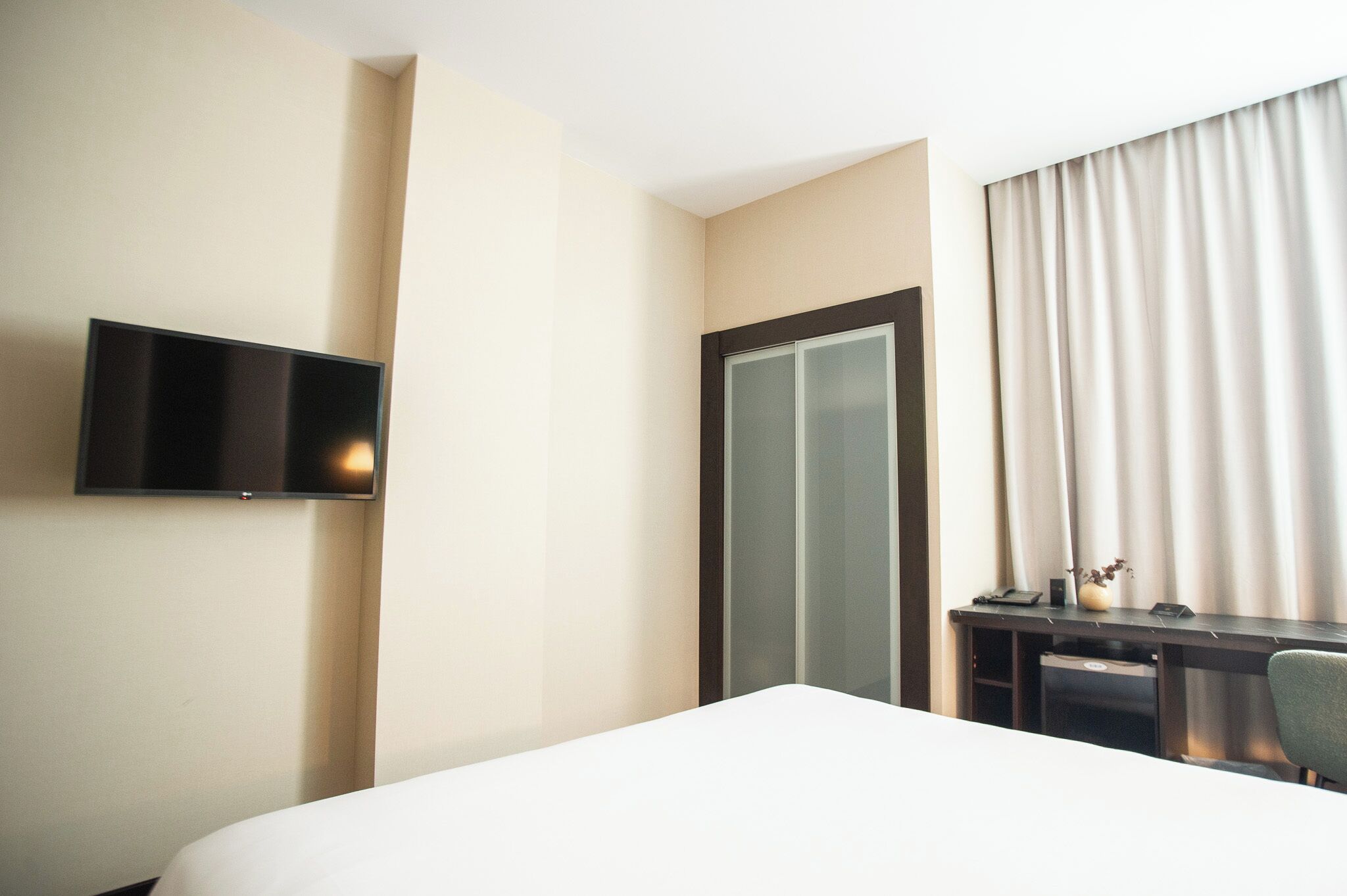 Une chambre d’hôtel comprenant un lit, un bureau avec un ordinateur, un téléviseur fixé au mur et une porte coulissante.