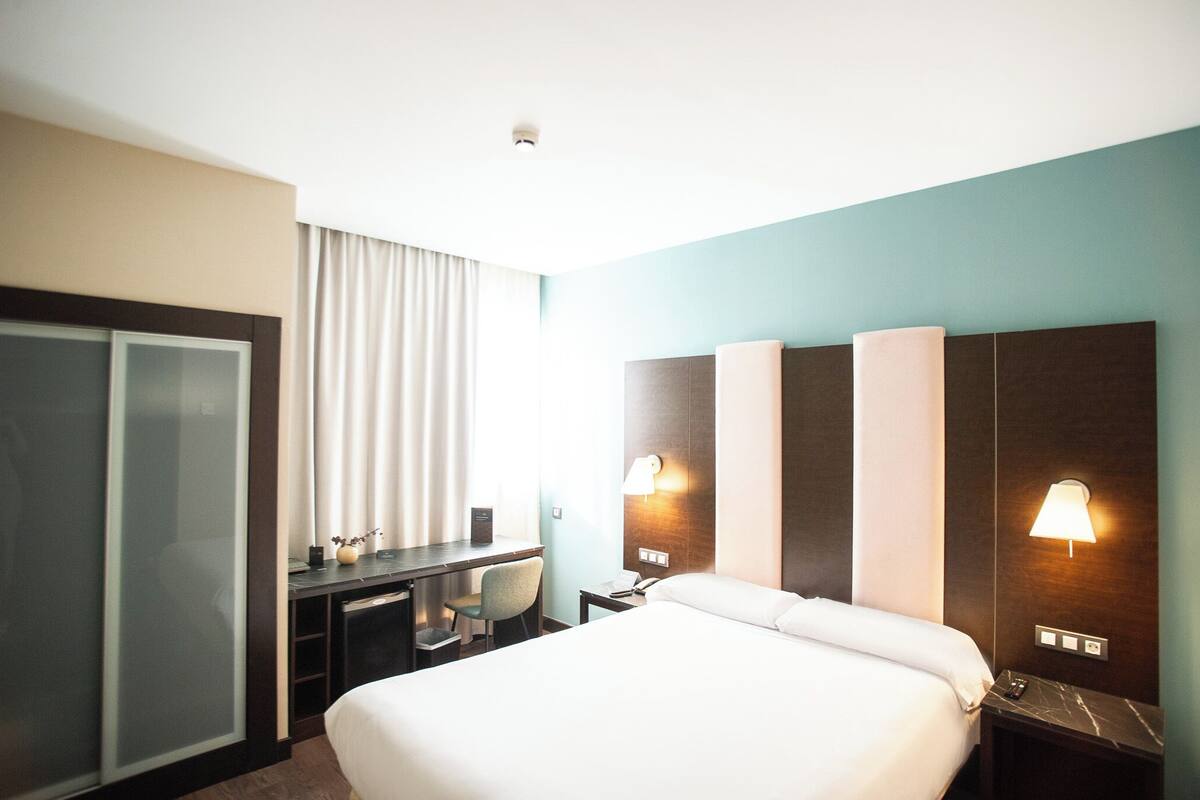 A hotel room with a bed, desk, chair, and a wardrobe.