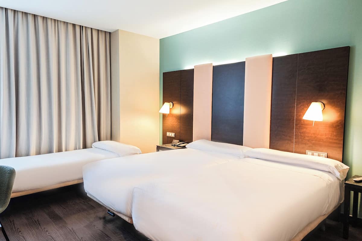 A hotel room with a large bed, two bedside tables, a chair, and a curtain.