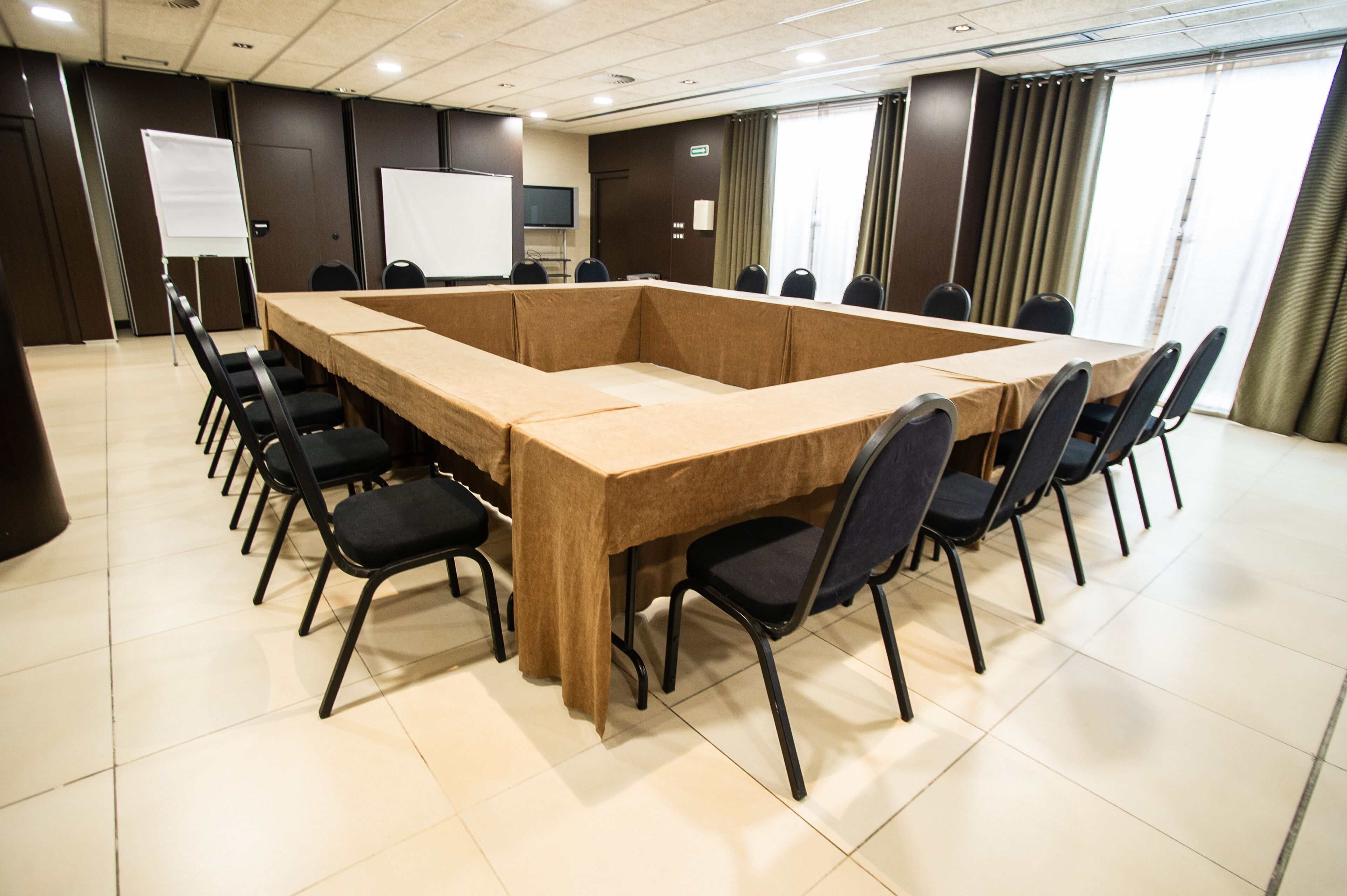 Een vergaderruimte met een grote rechthoekige tafel, omringd door stoelen, een whiteboard en een televisie.