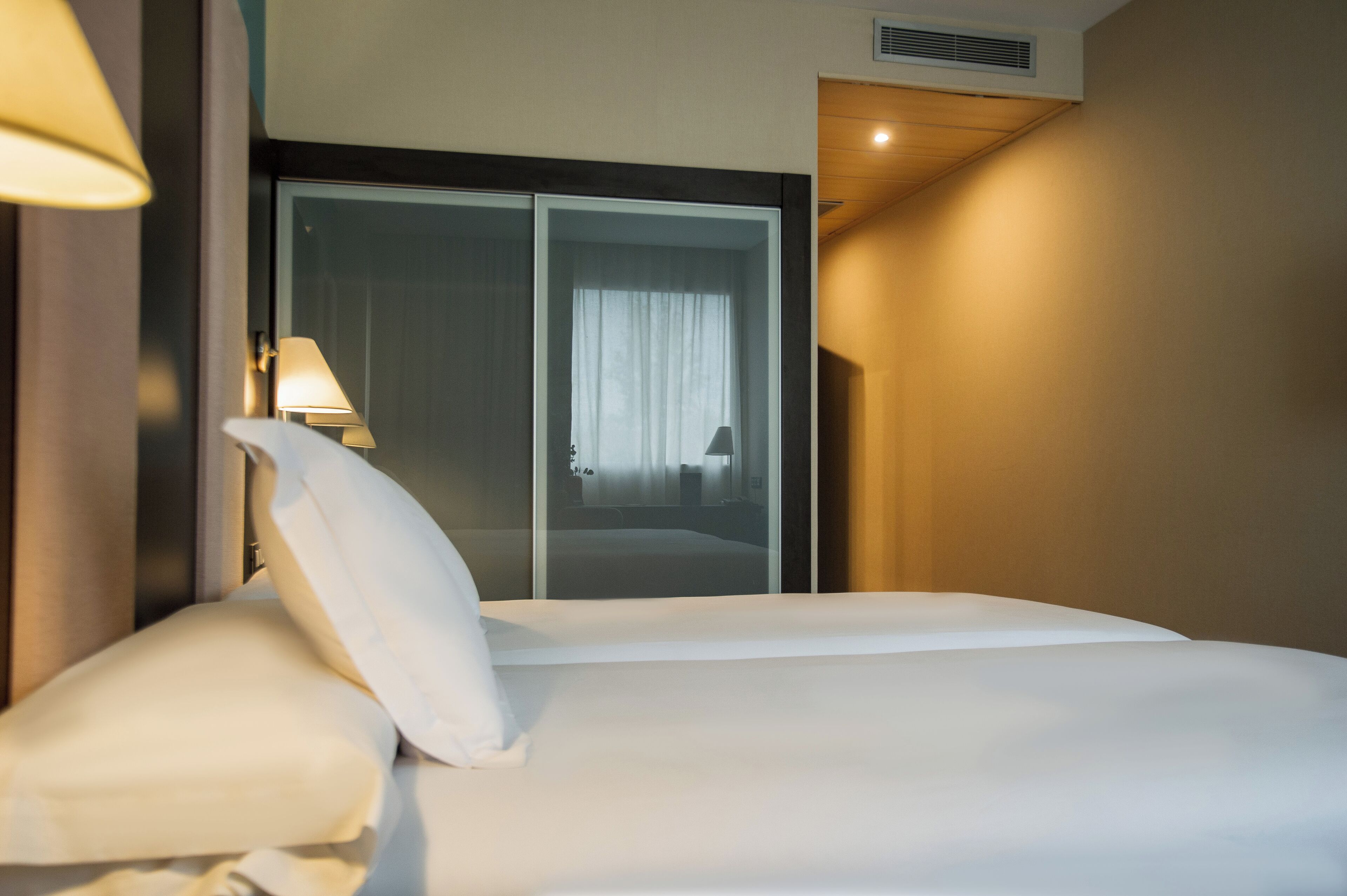 Habitación de hotel con una cama grande, armario corredero, lámpara de noche y rejilla de ventilación en la pared.