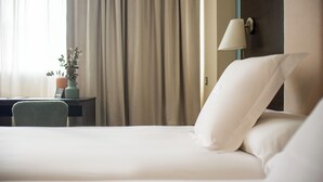 Hotellihuone, jossa on sänky, työpöytä, lamppu ja ruukussa oleva kasvi.